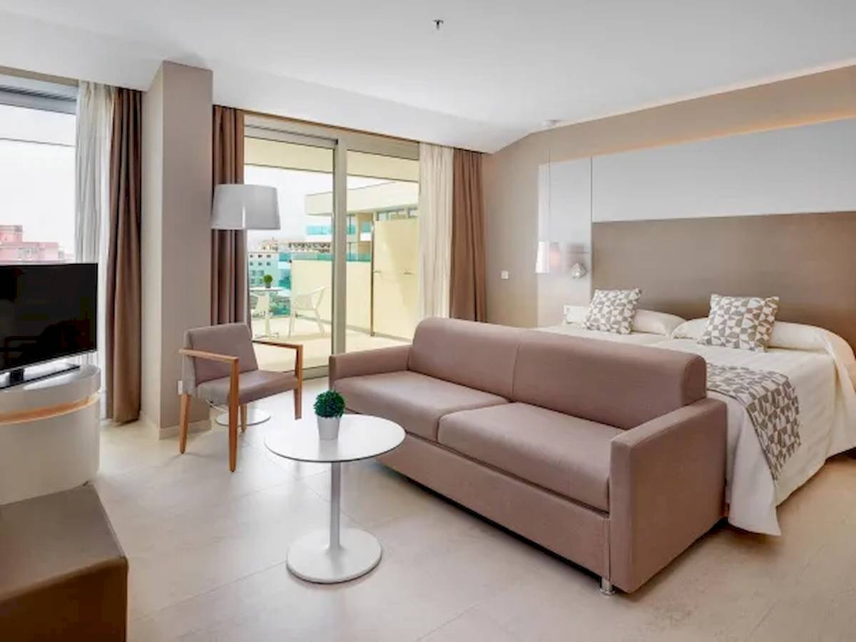 Innenansicht der Suite im Hotel Hipotels Gran Playa de Palma mit Bett, Sofa, Tisch und Fernseher.