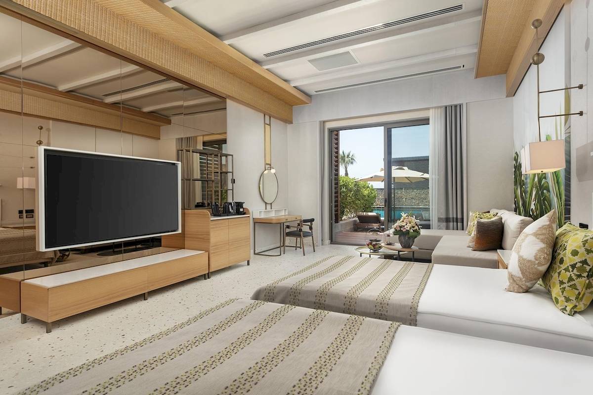 Innenansicht eines Gästezimmers im Cullinan Belek Hotel mit Fernseher, Schreibtisch und Poolblick.