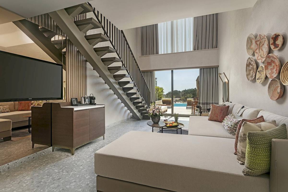 Wohnbereich des Cullinan Belek Hotels mit großem Sofa, Fernseher und einer Treppe.