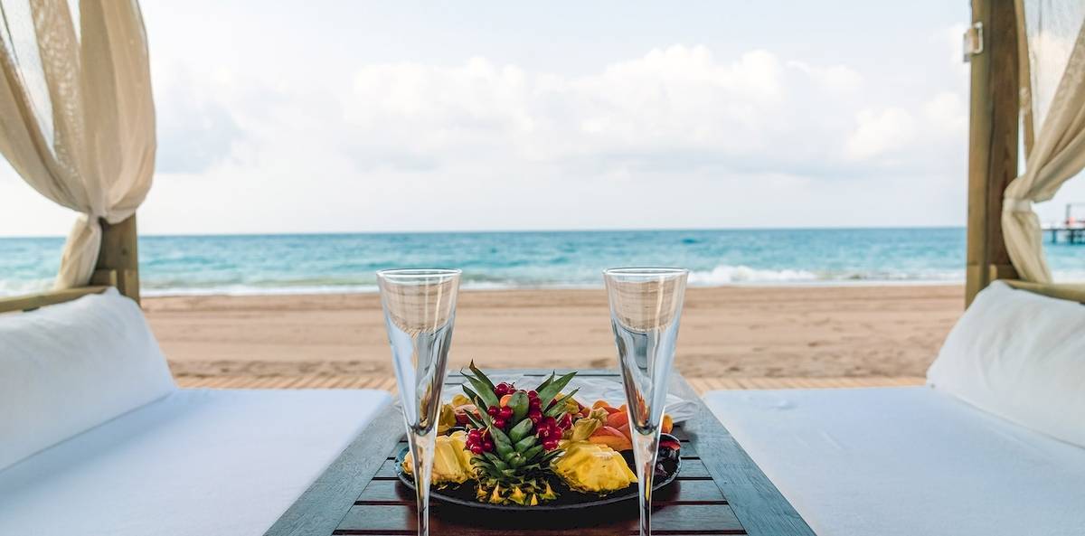 Zwei Liegesessel am Strand mit Gläsern und einer Obstplatte.