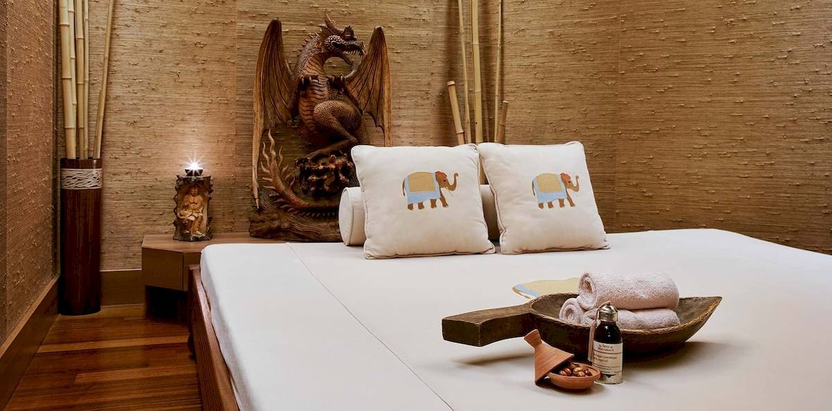 Bett im Gloria Golf Resort Spa mit weißen Laken, zwei Kissen mit Elefantenmuster und einem Holztablett mit Gegenständen.