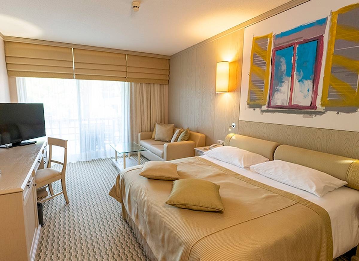 Hotelzimmer im Gloria Golf Resort mit Doppelbett, Fernseher, Sofa und Couchtisch.