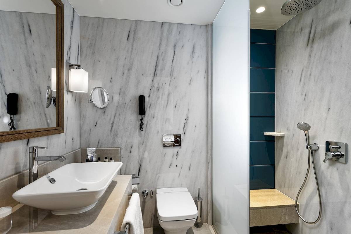 Badezimmer im Titanic Luxury Collection Bodrum Hotel mit Marmorwänden, Dusche, Toilette und Waschbecken.