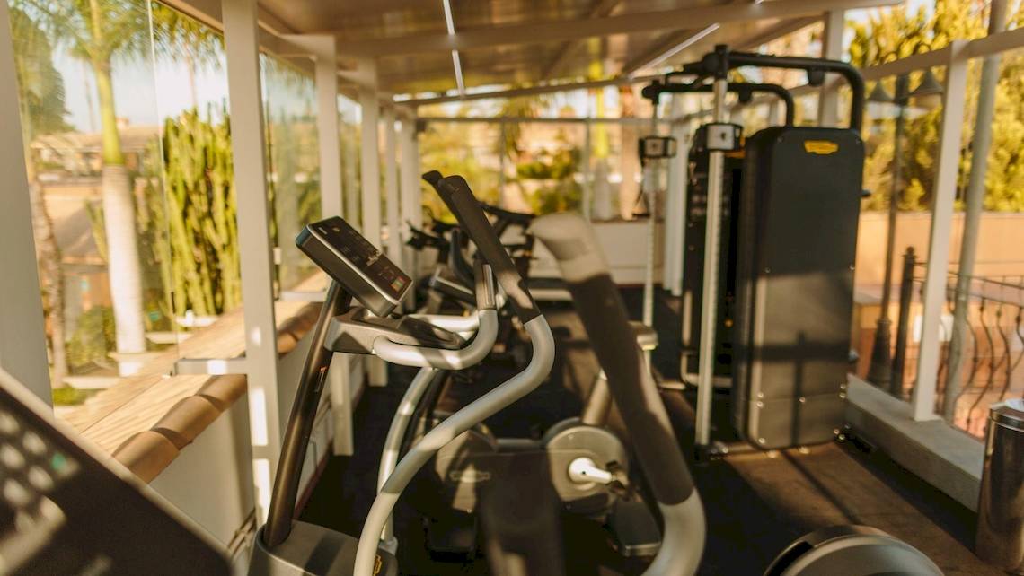 Fitnessraum im Suites & Villas By Dunas Hotel mit Cardiogeräten und Blick auf den Garten.