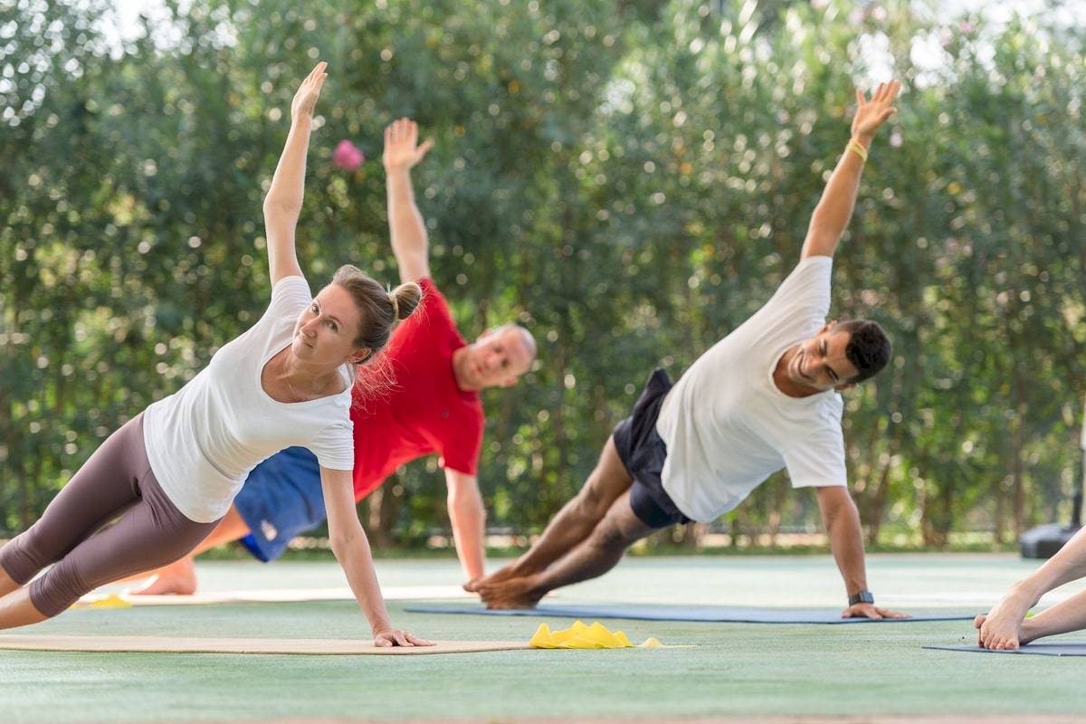 Yoga-Übungen im Freien im Xanadu Resort Hotel mit drei Personen, die verschiedene Positionen einnehmen.