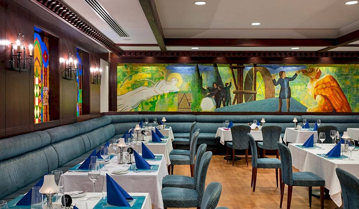 Innenansicht des Restaurants im Xanadu Resort Hotel mit einer großen Wandmalerei, blauen Sitzbankreihen und gedeckten Tischen.