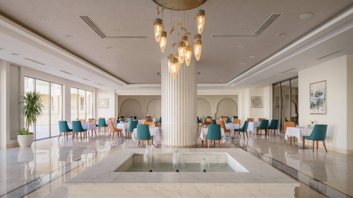 Innenbereich des Xanadu Makadi Bay Hotels mit modernem Restaurant, Wasserbrunnen und vielen Tischen und Stühlen.