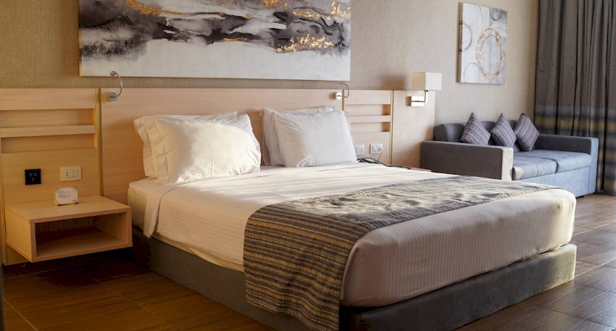 Hotelzimmer im Xanadu Makadi Bay mit zwei Betten, Kissen, einem Tisch, einer Couch und Kunstwerken an der Wand.