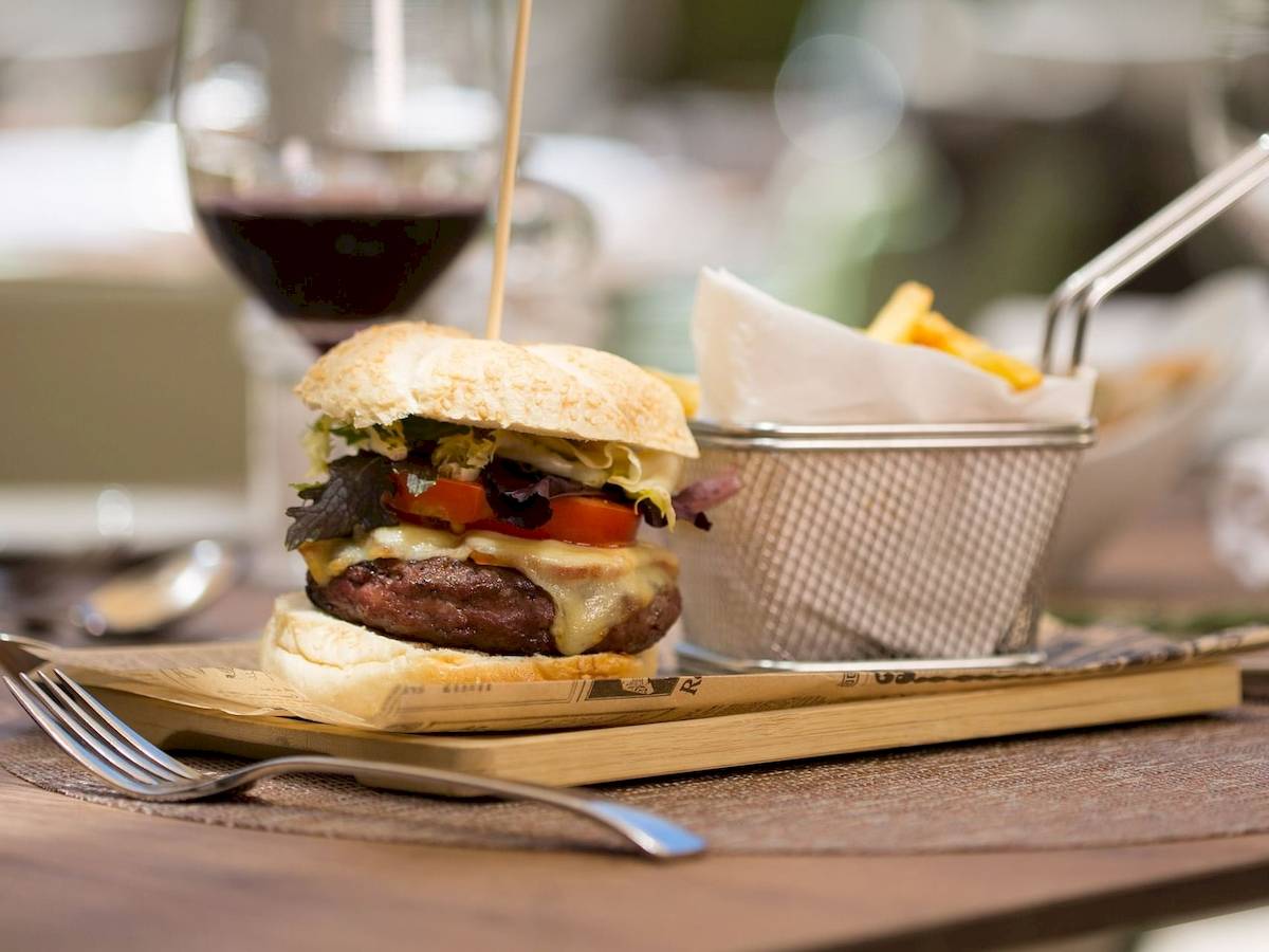 Ein Burger mit Pommes auf einer Holzplatte im Aimia Hotel.
