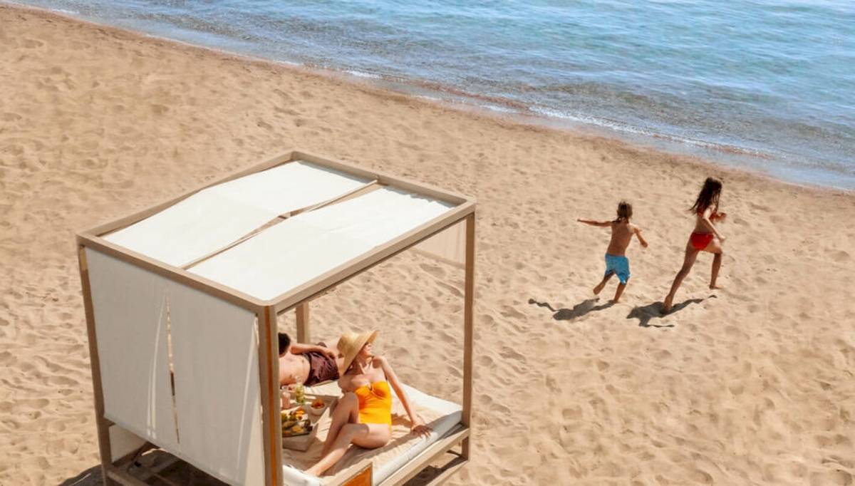 Familie genießt den Strandbereich im Ikos Dassia Hotel, mit Sonnenliege und spielenden Kindern.