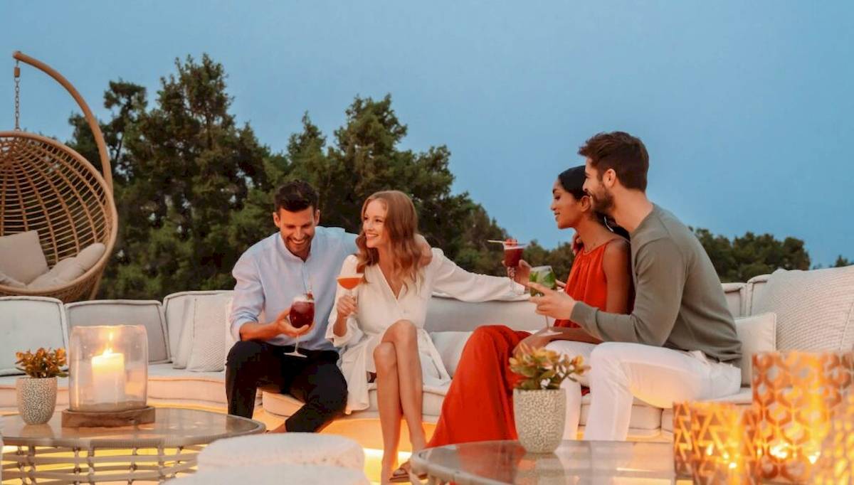 Vier Gäste sitzen im Freien und genießen Cocktails auf dem Ikos Dassia Hotel.