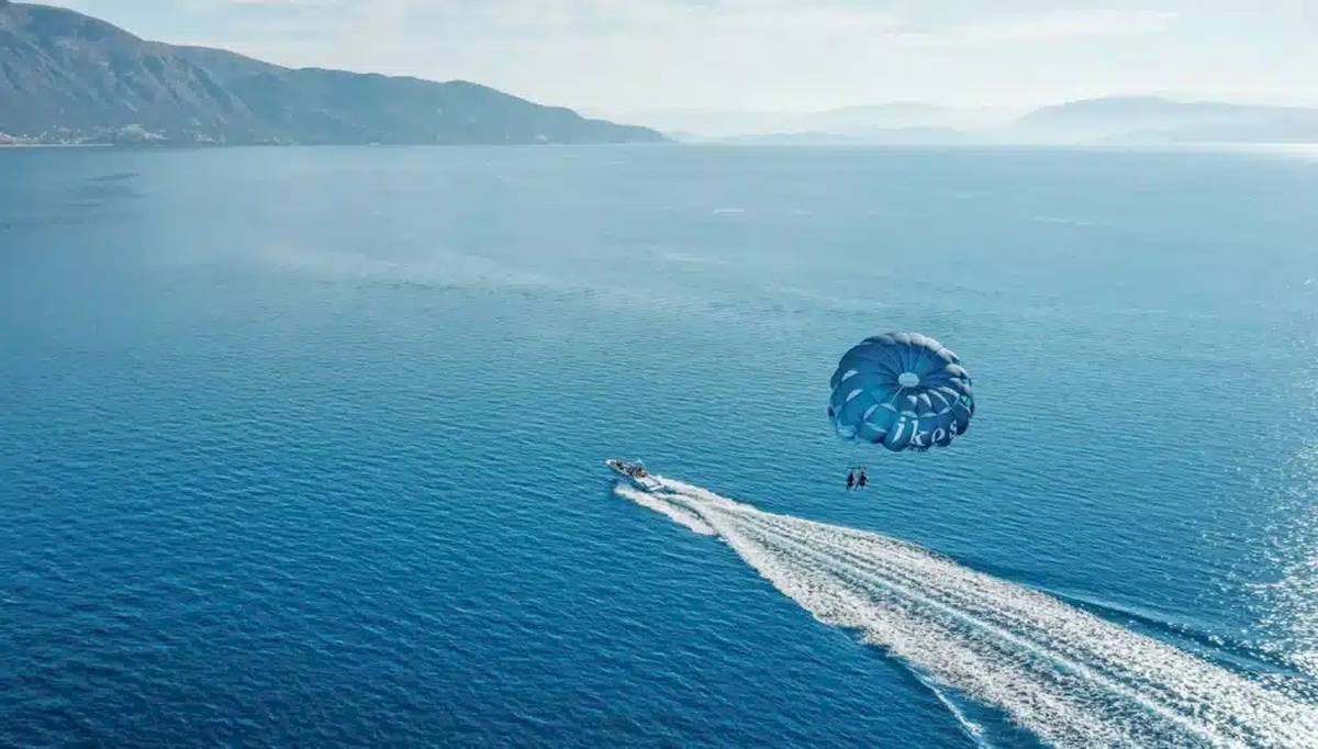 Zwei Personen parasailing über dem Meer vor dem Ikos Dassia Hotel.