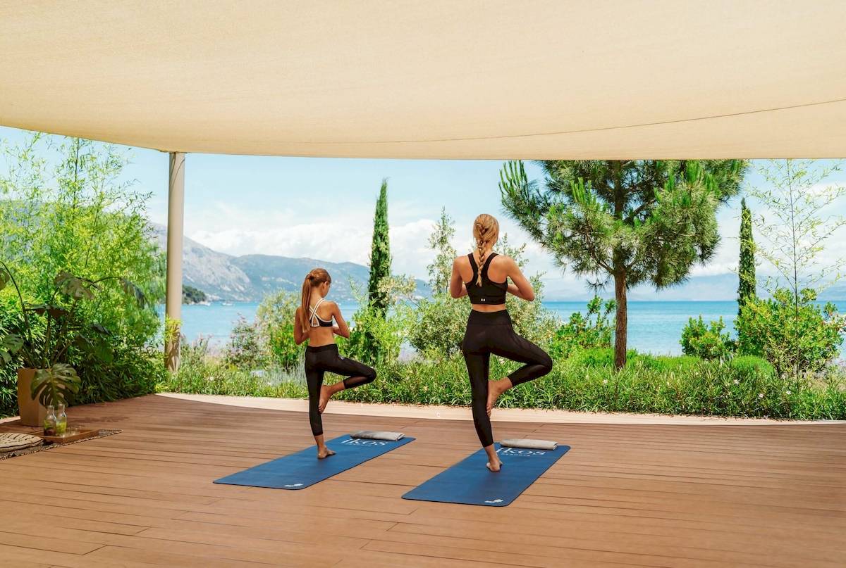 Zwei Frauen machen Yoga auf einem Holzboden mit Meerblick im Ikos Dassia Hotel.