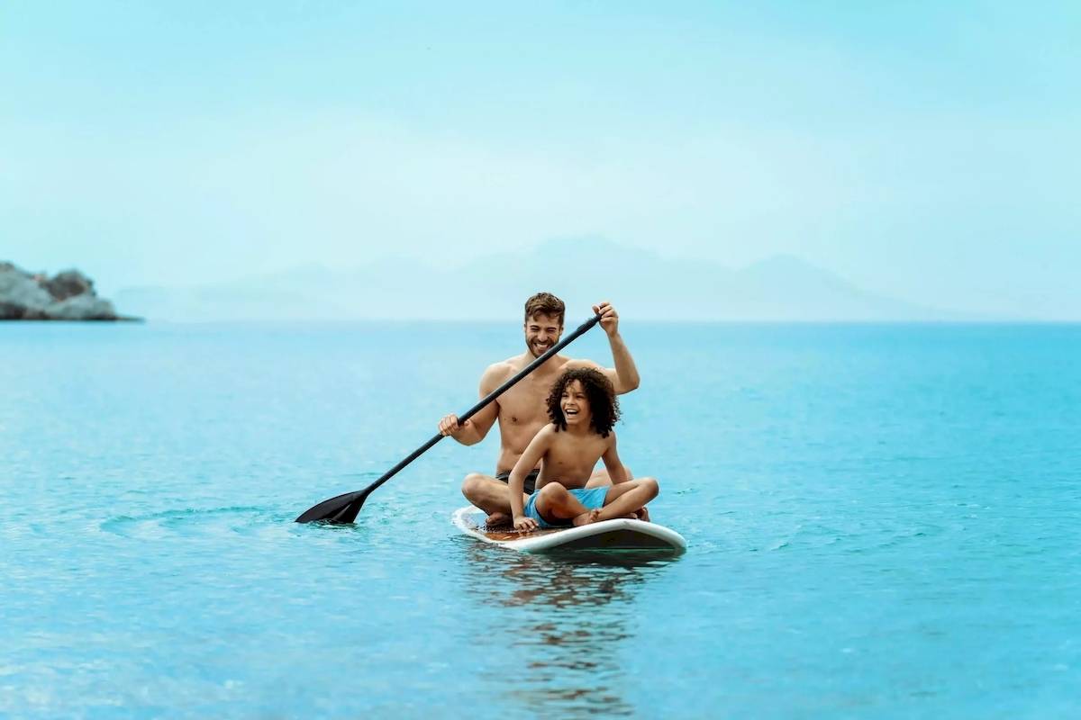 Mann und Junge paddeln auf einem Surfbrett im Meer.