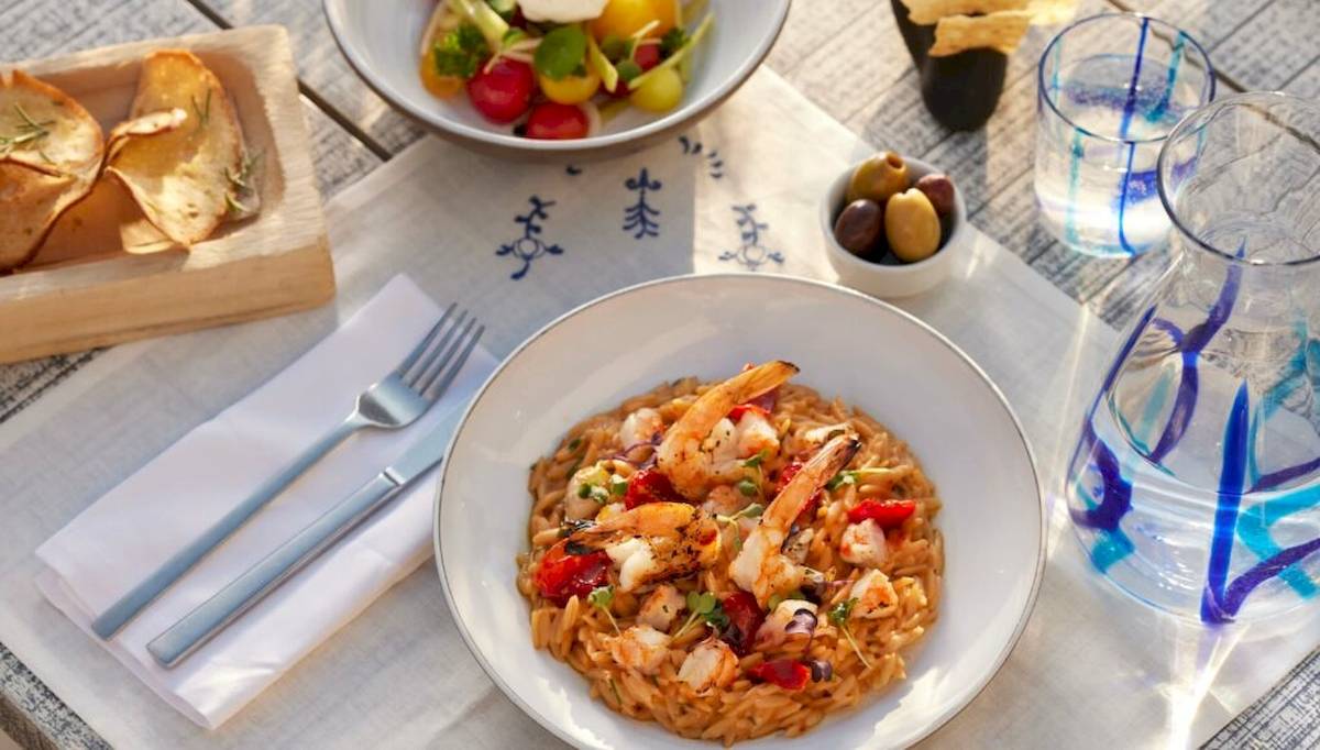 Ein Teller mit Garnelen und Reis steht auf einem Tisch mit Salat, Oliven und Trinkgläsern.