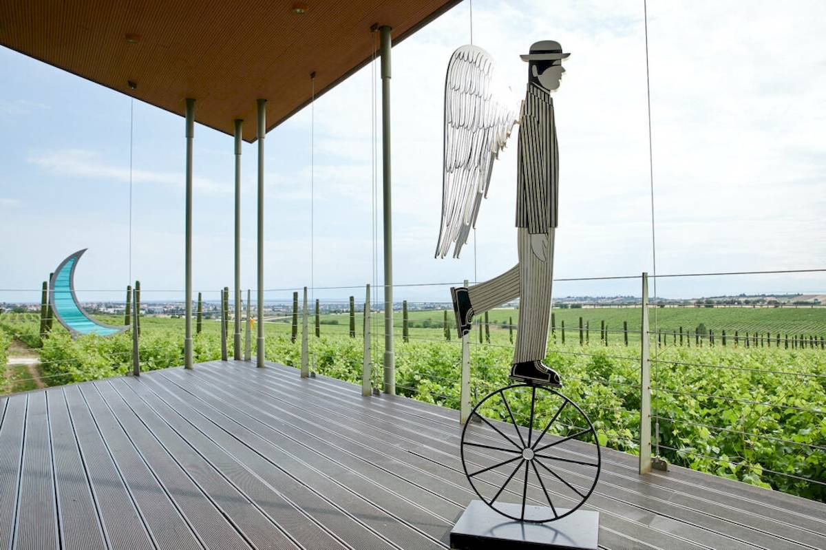 Statue eines Mannes auf Einrad auf Terrasse vor Weinberg bei Ikos Olivia Hotel