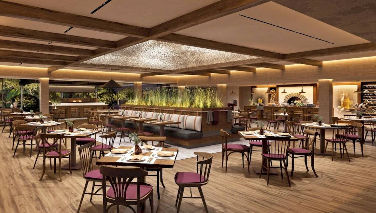 Innenansicht des Restaurants im Ikos Porto Petro Hotel mit Holztischen und Stühlen, Pflanzen und hoher Decke.