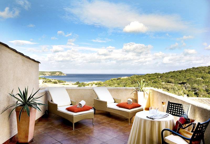 Außenterrasse des CPH Pevero Hotels mit zwei Loungesesseln, einem Tisch und einem Blick auf das Meer.