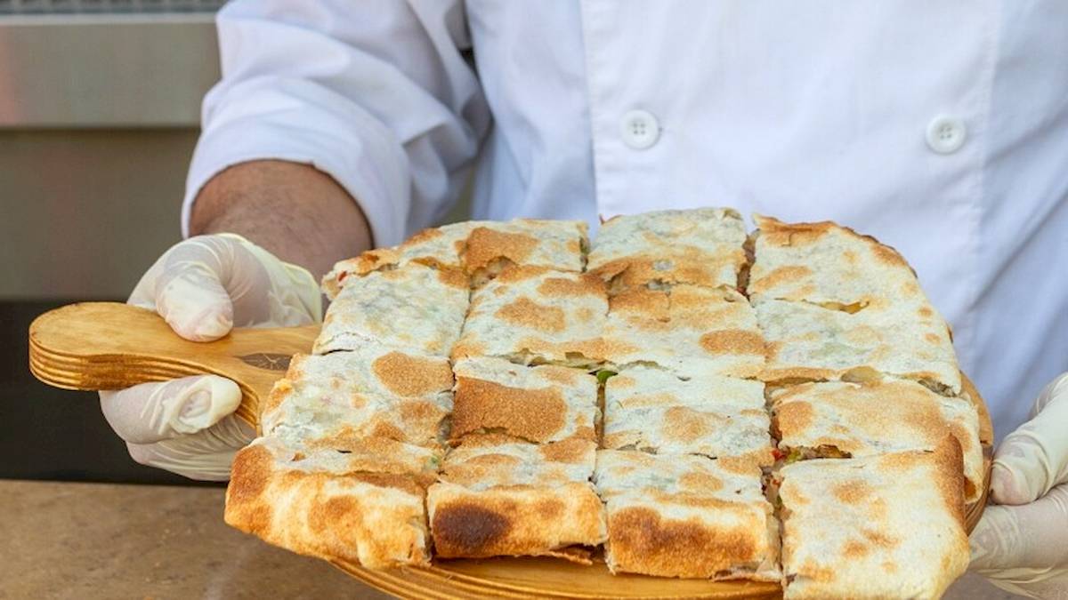 Koch hält ein geschnittenes Pizzabrot auf einem Holzbrett.