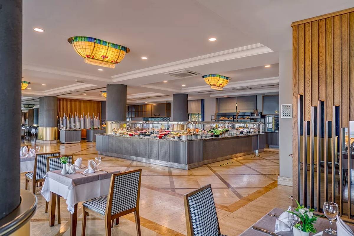 Innenansicht des Restaurants im Melas Resort mit Buffet, Tischen und Stühlen.