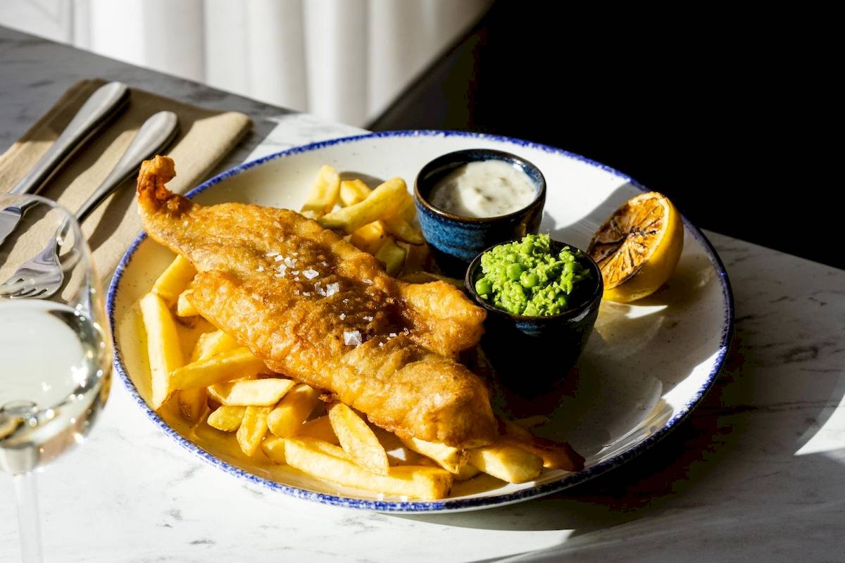 Fisch und Chips Gericht auf Teller mit Pommes und Saucen.