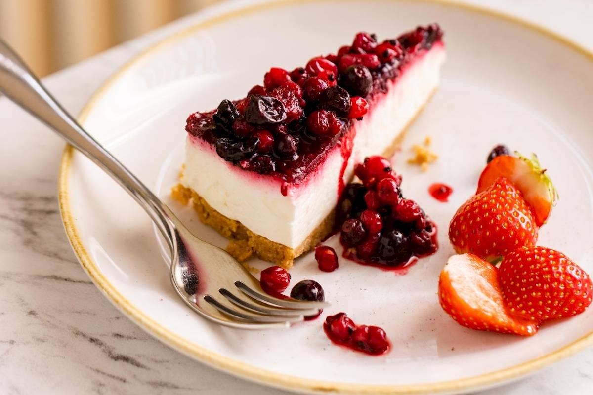 Ein Stück Schokoladenkuchen mit Beeren und Erdbeeren auf einem weißen Teller mit einer Gabel daneben.