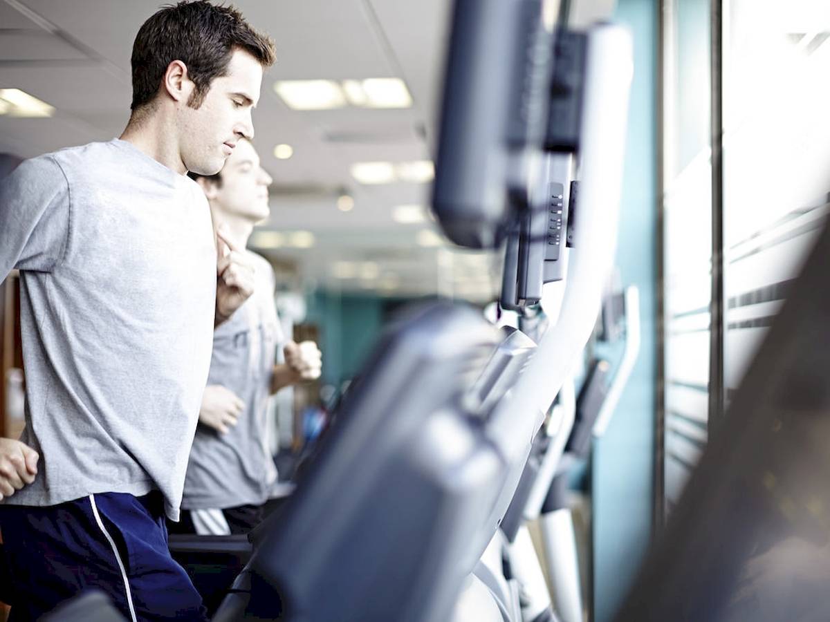 Ein Mann läuft auf einem Laufband im Fitnessstudio, während ein anderer Mann im Hintergrund läuft.