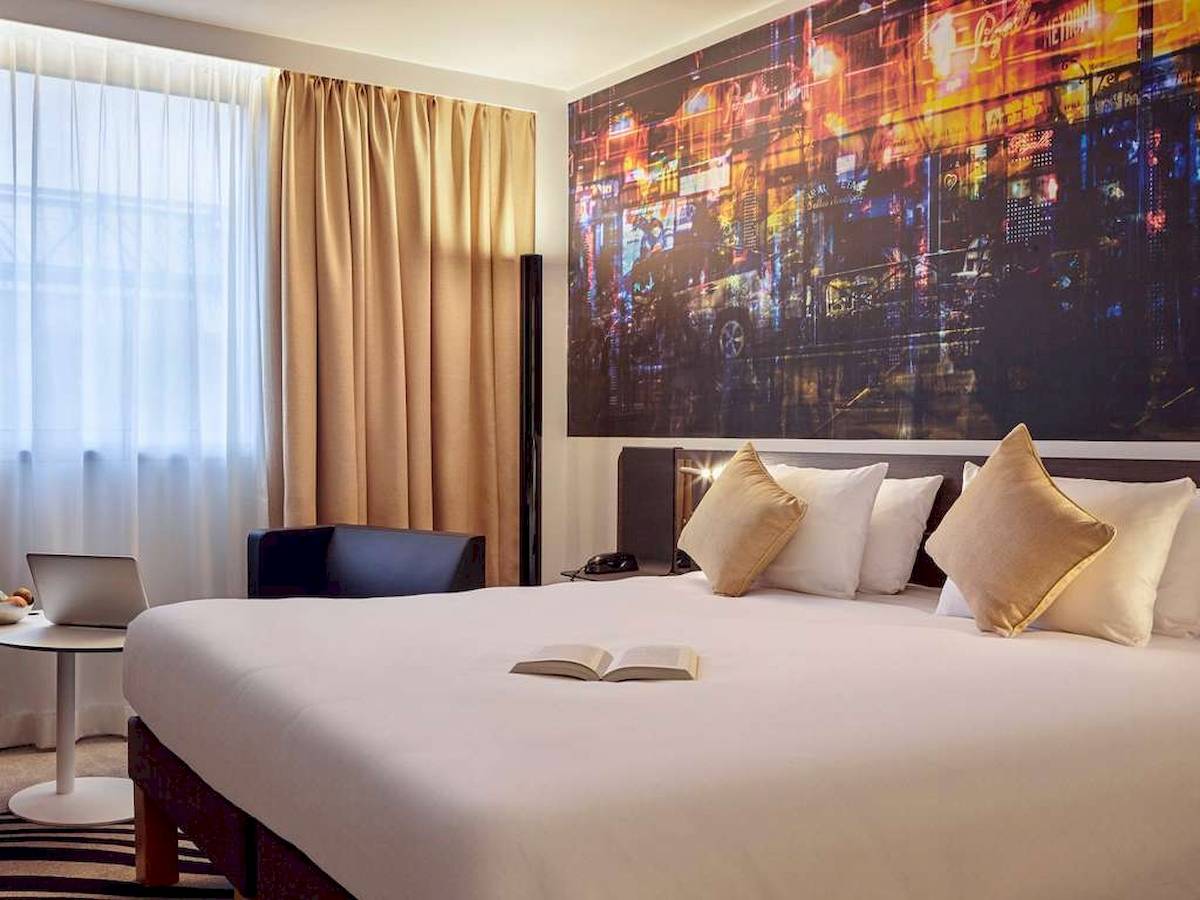 Hotelzimmer im Novotel Paris Centre Bercy mit großem Bett, offenem Buch und Laptop.