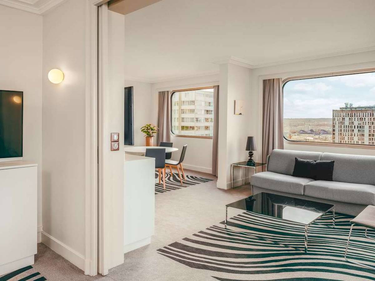 Innenansicht des Wohnbereichs im Novotel Paris Tour Eiffel mit Sofa, Tisch und Blick auf die Stadt