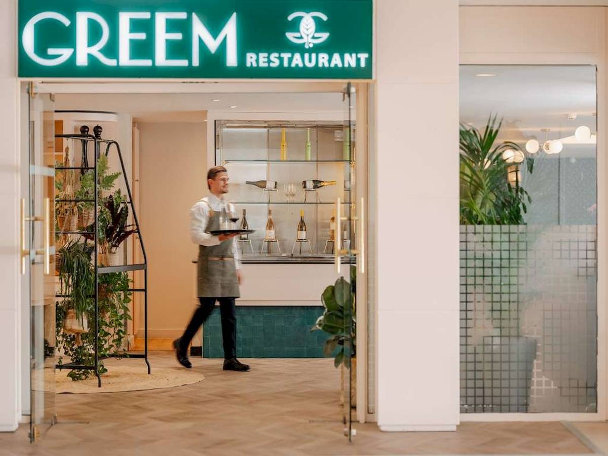 Eingang des Greem Restaurants im Novotel Paris Tour Eiffel mit Kellner, der Flaschen und Weingläser präsentiert.