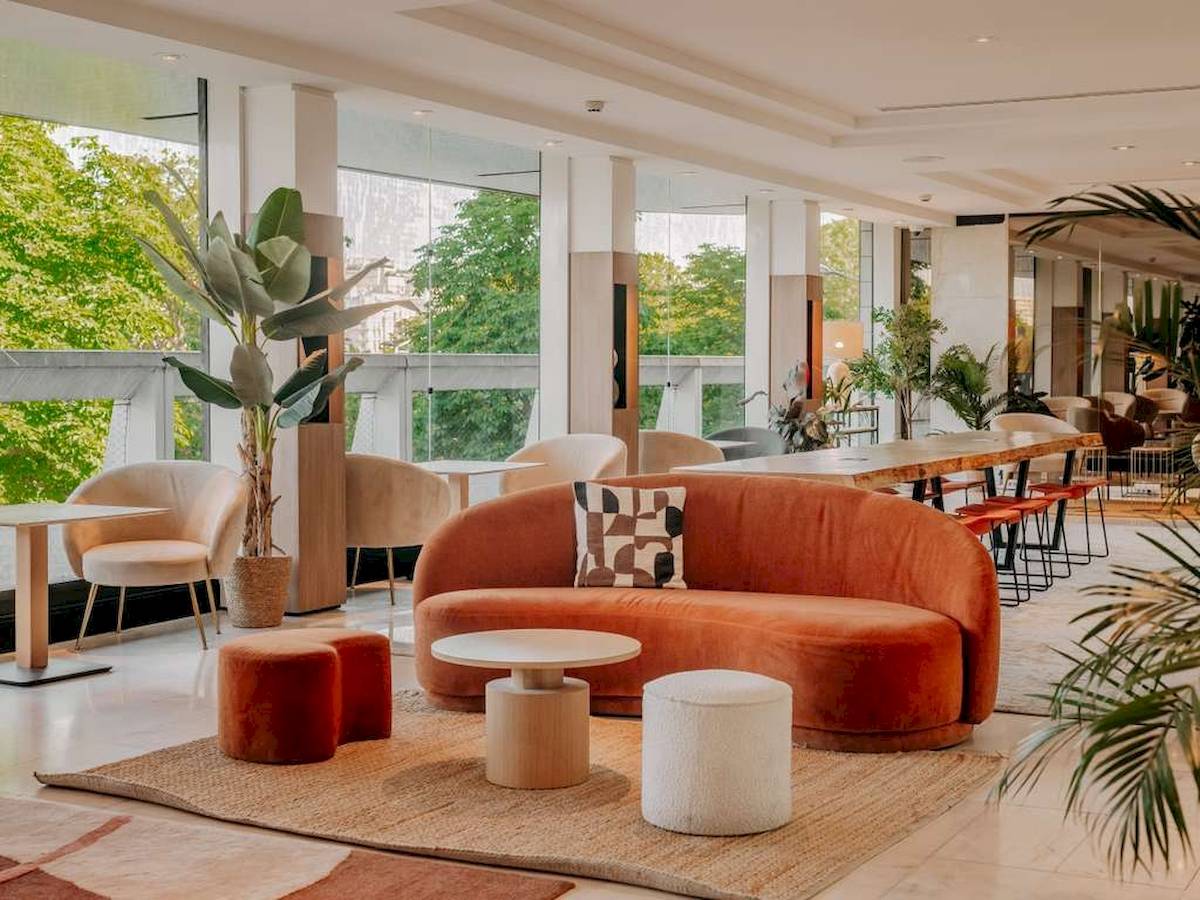 Innenbereich des Novotel Paris Tour Eiffel mit modernem Möbeldesign, großen Fenstern und Blick auf Bäume draußen.