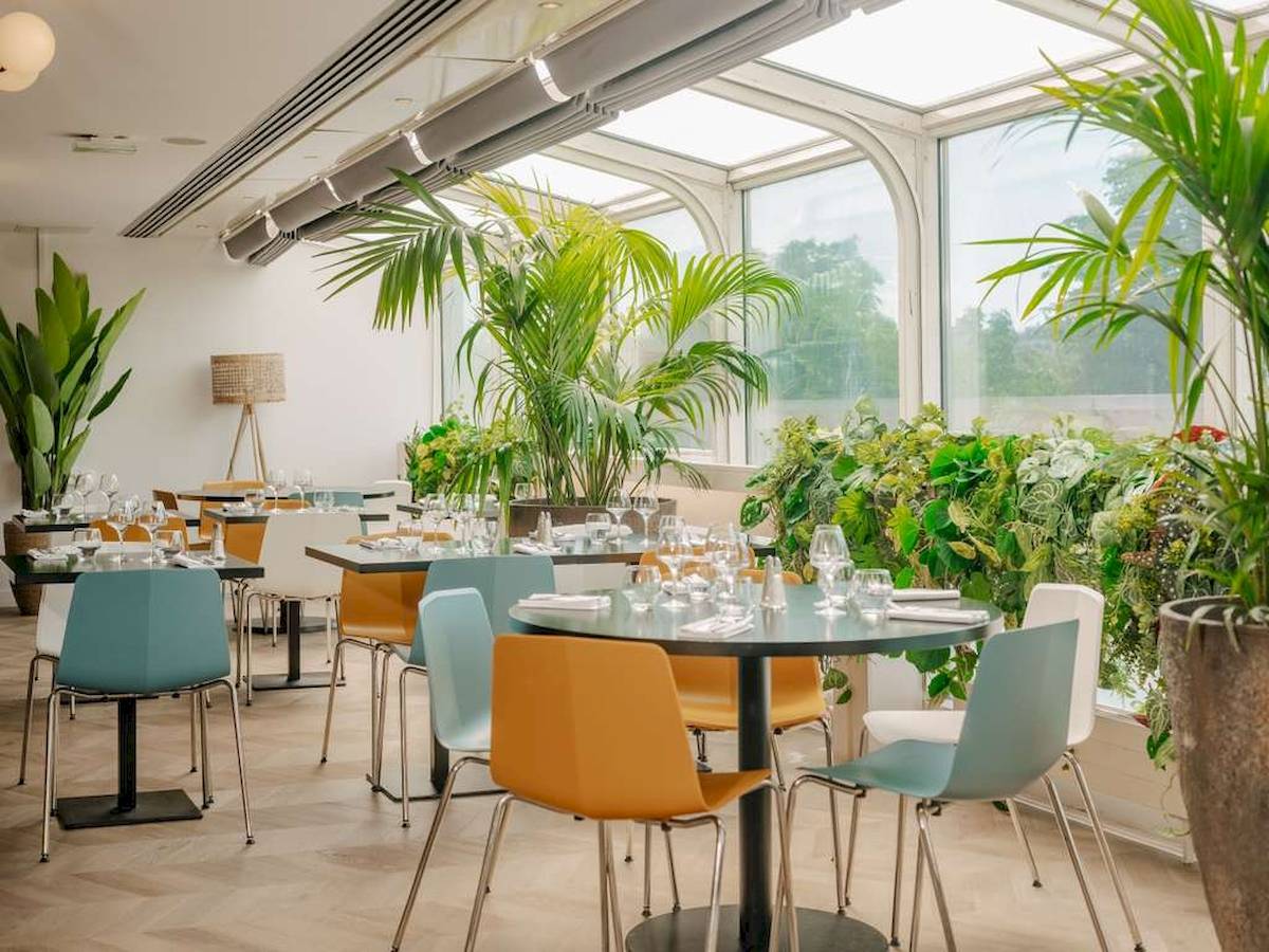 Innenansicht des Restaurants im Novotel Paris Tour Eiffel mit runden Tischen, farbenfrohen Stühlen und großen Fenstern.