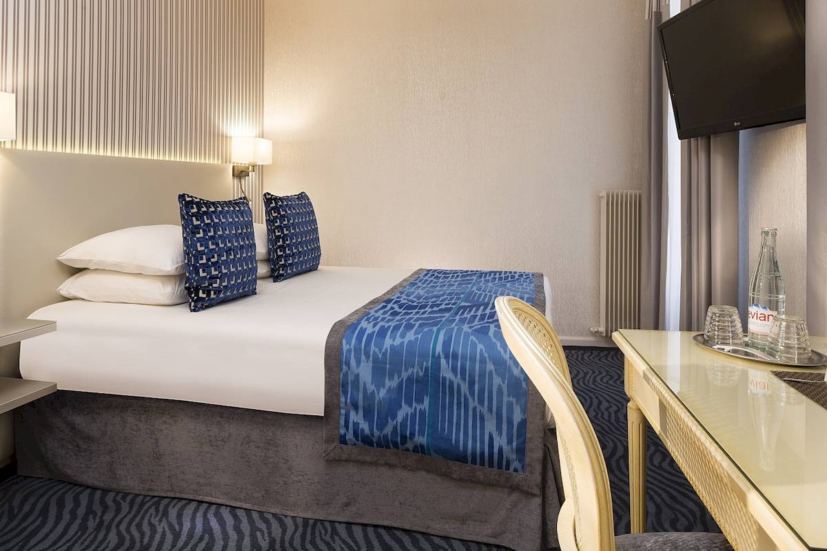 Hotelzimmer im Victor Hugo Paris Kléber mit Bett, Kissen, Schreibtisch und Fernseher.