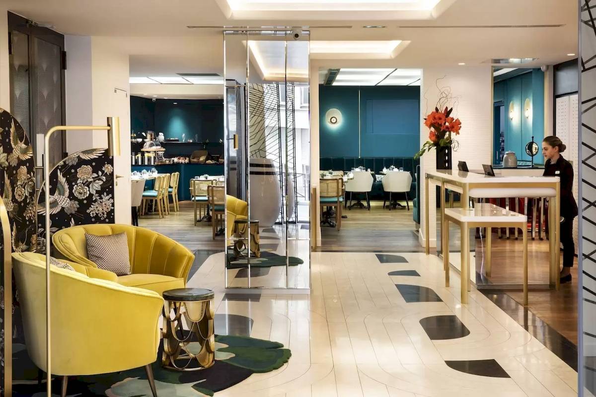 Innenansicht des Victor Hugo Paris Kléber Hotels mit Rezeption, gelben Stühlen und blauen Wänden.