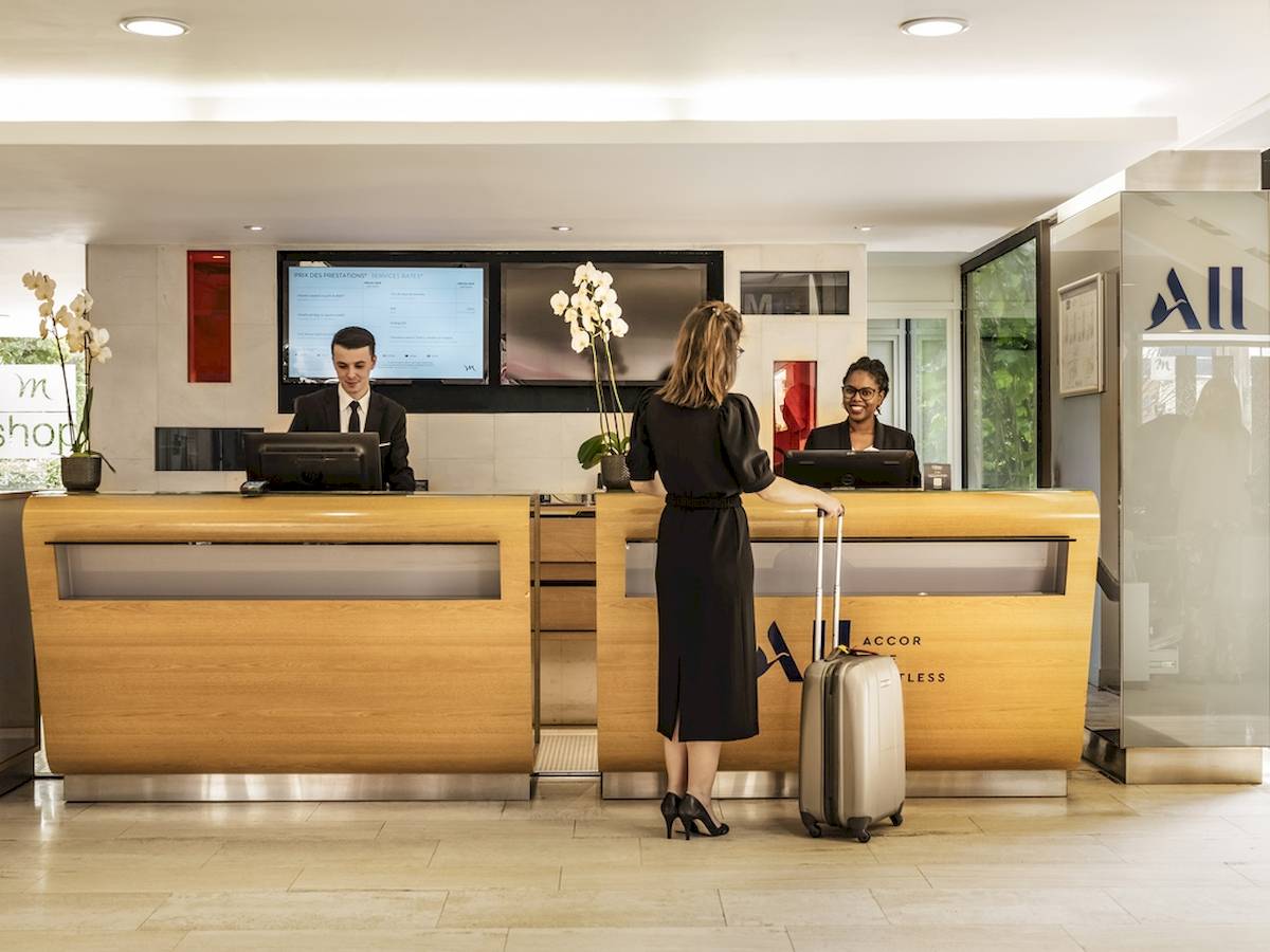 Rezeption im Mercure Paris Centre Tour Eiffel Hotel mit einer Frau, die einen Koffer zieht.