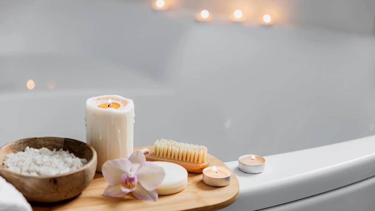 Eine Badewanne mit Kerzen, Seife, einer Orchidee und einem Handschuh in einem ruhigen Badezimmer.