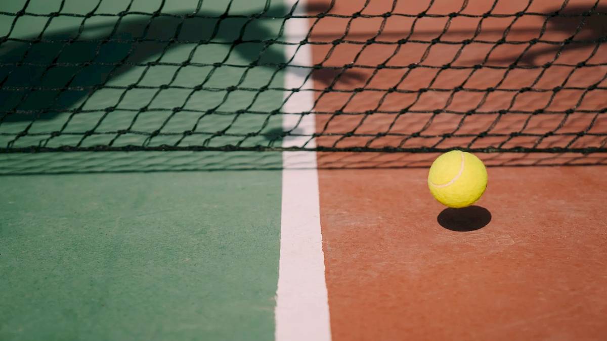 Ein gelber Tennisball liegt auf einem Tennisplatz neben dem Netz.