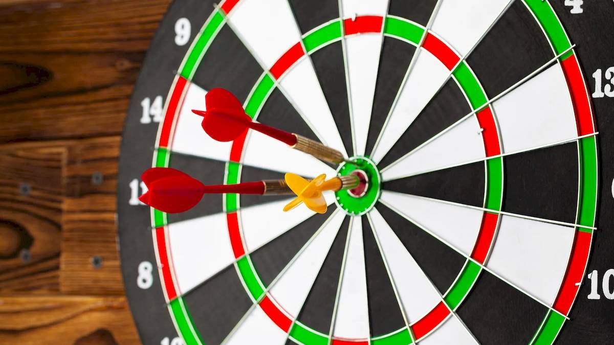 Dartscheibe mit zwei roten und einem gelben Pfeil auf einem hölzernen Hintergrund.