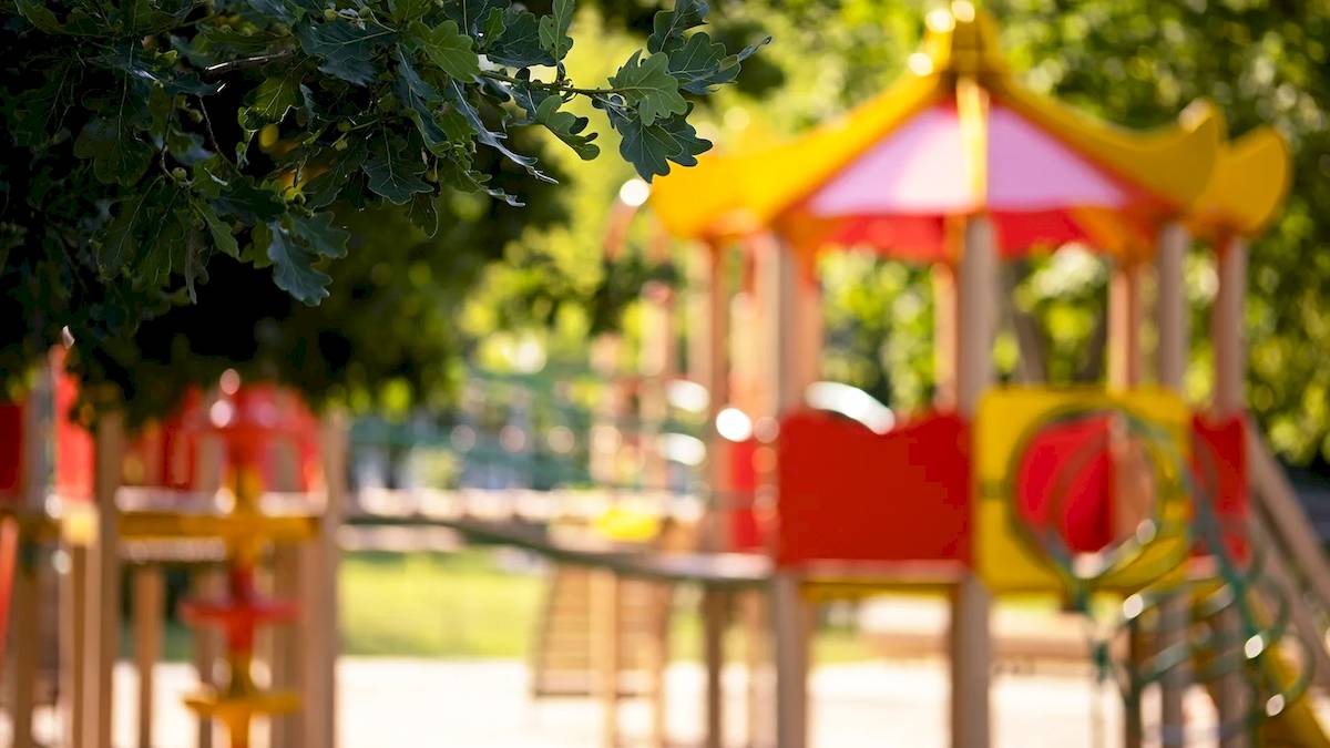 Foto eines bunten Kinderspielplatzes im Freien mit Bäumen im Hintergrund.