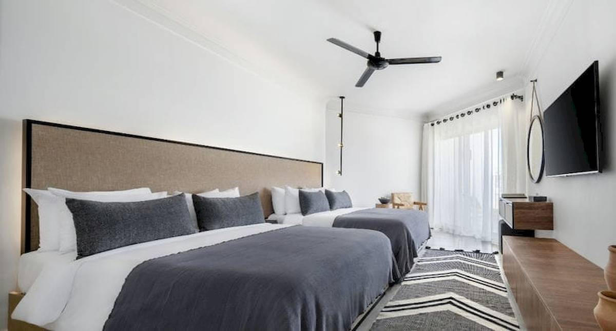 Zwei moderne Schlafzimmer im Serry Beach Resort mit weißen Wänden, Deckenventilator, Fernseher und Bettwäsche.