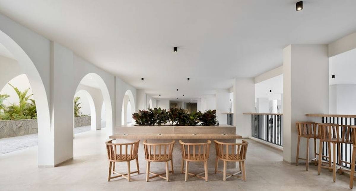 Innenbereich des Serry Beach Resort mit weißem Wanddesign, hölzernen Stühlen und Tischen, und grünen Pflanzen.