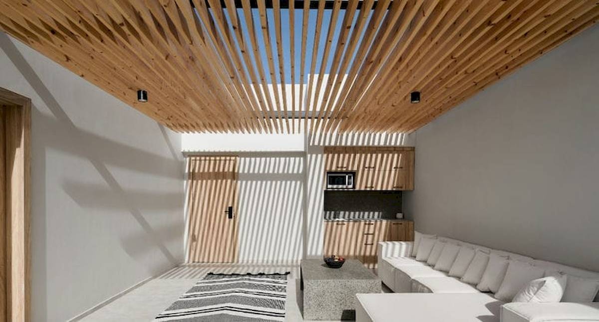 Innenraum des Serry Beach Resorts mit weißen Wänden, Holzdecke, Couch, Teppich und Küchenbereich.
