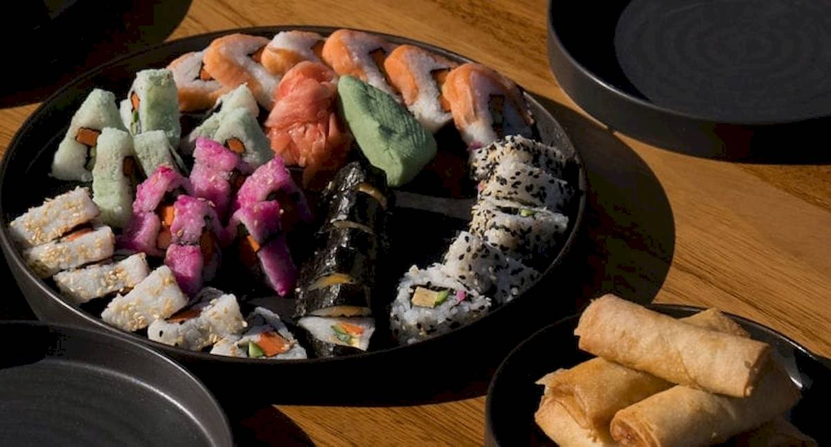 Ein großer Teller mit verschiedenen Sushi-Rollen und Springrollen auf einem Holztisch.