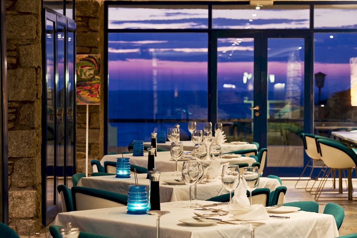 Das Innenrestaurant des Mykonos Theoxenia Boutique Hotels mit gedeckten Tischen und Blick auf den Abendhimmel.