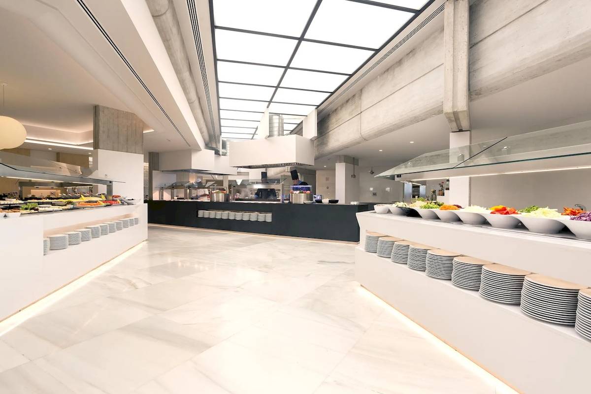 Innenansicht des Restaurants im Hipotels Mediterraneo mit Speisenbuffet und Glasüberdachungen.