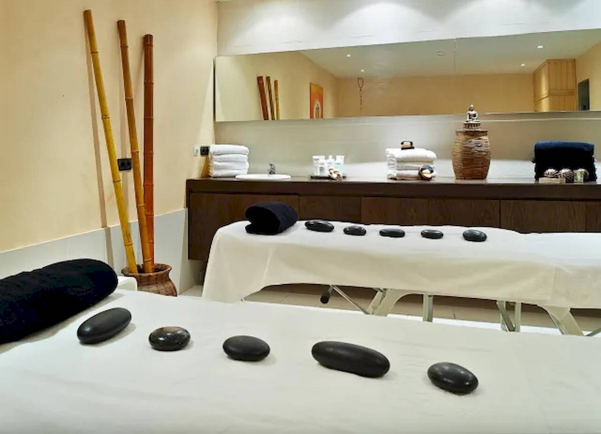 Spa-Behandlungsraum im Hipotels Mediterraneo mit zwei Massagetischen, schwarzen Steinen und einem großen Spiegel.