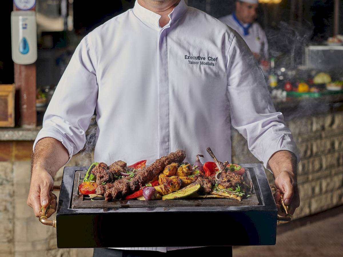 Executive Chef Tamer Mostafa hält eine Grillplatte mit verschiedenen gegrillten Gerichten.
