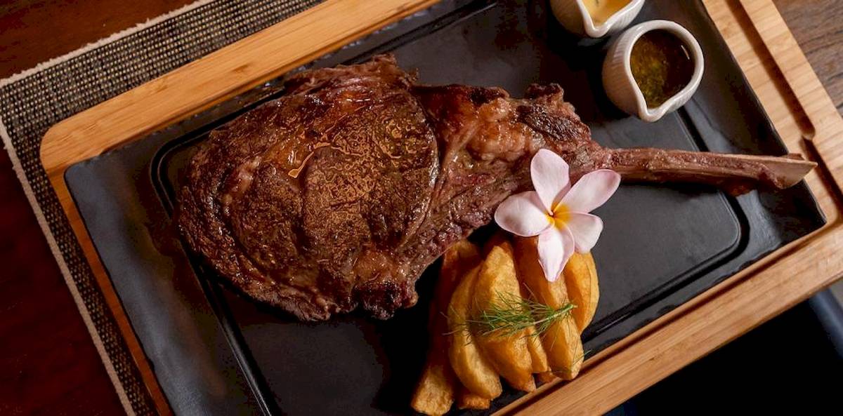 Ein gegrilltes Steak mit Rosmarin und Blumen auf einem schwarzen Teller.