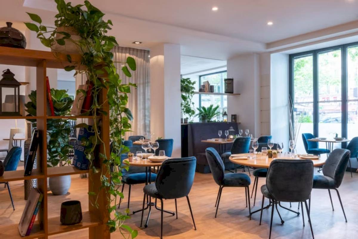 Innenansicht des Restaurants im Crowne Plaza Paris République mit runden Tischen, blauen Stühlen und Pflanzen.