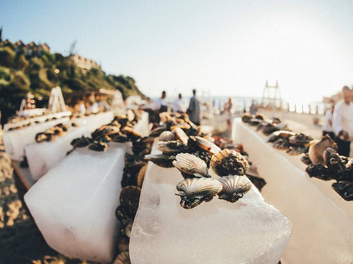 Ein Bild von Meeresfrüchten auf Eisblöcken, die am Strand von Club Marvy angeordnet sind, mit einigen Leuten im Hintergrund.
